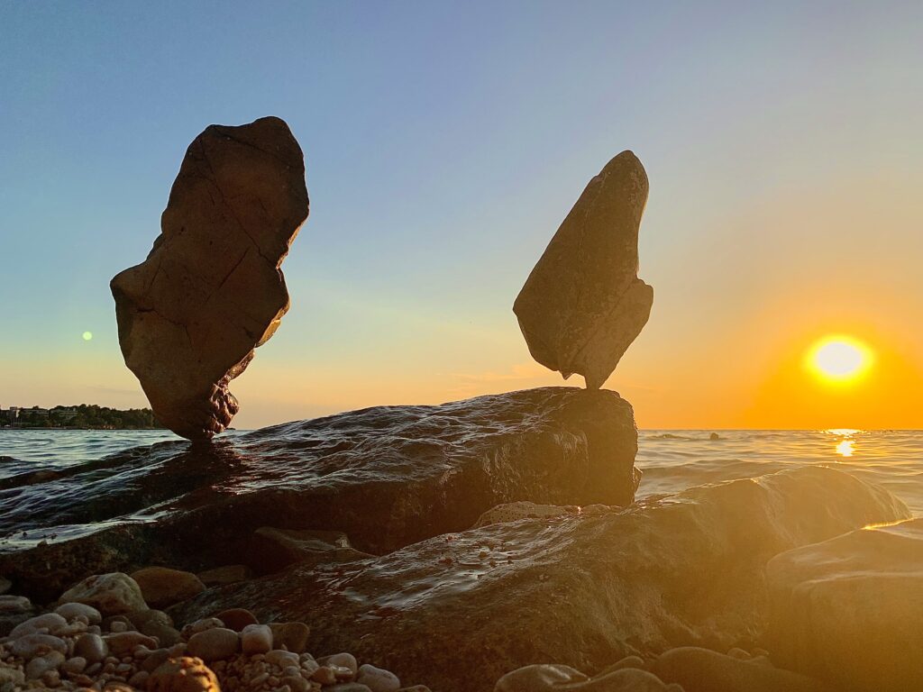 Zwei frei balancierte, kantige Steine auf einem Felsen im warmen Licht der tief stehenden Sonne.